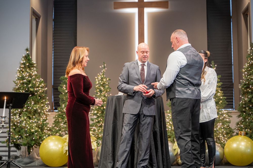 Wedding ceremony takes place in a church with illuminated cross and gold decorative spheres.
