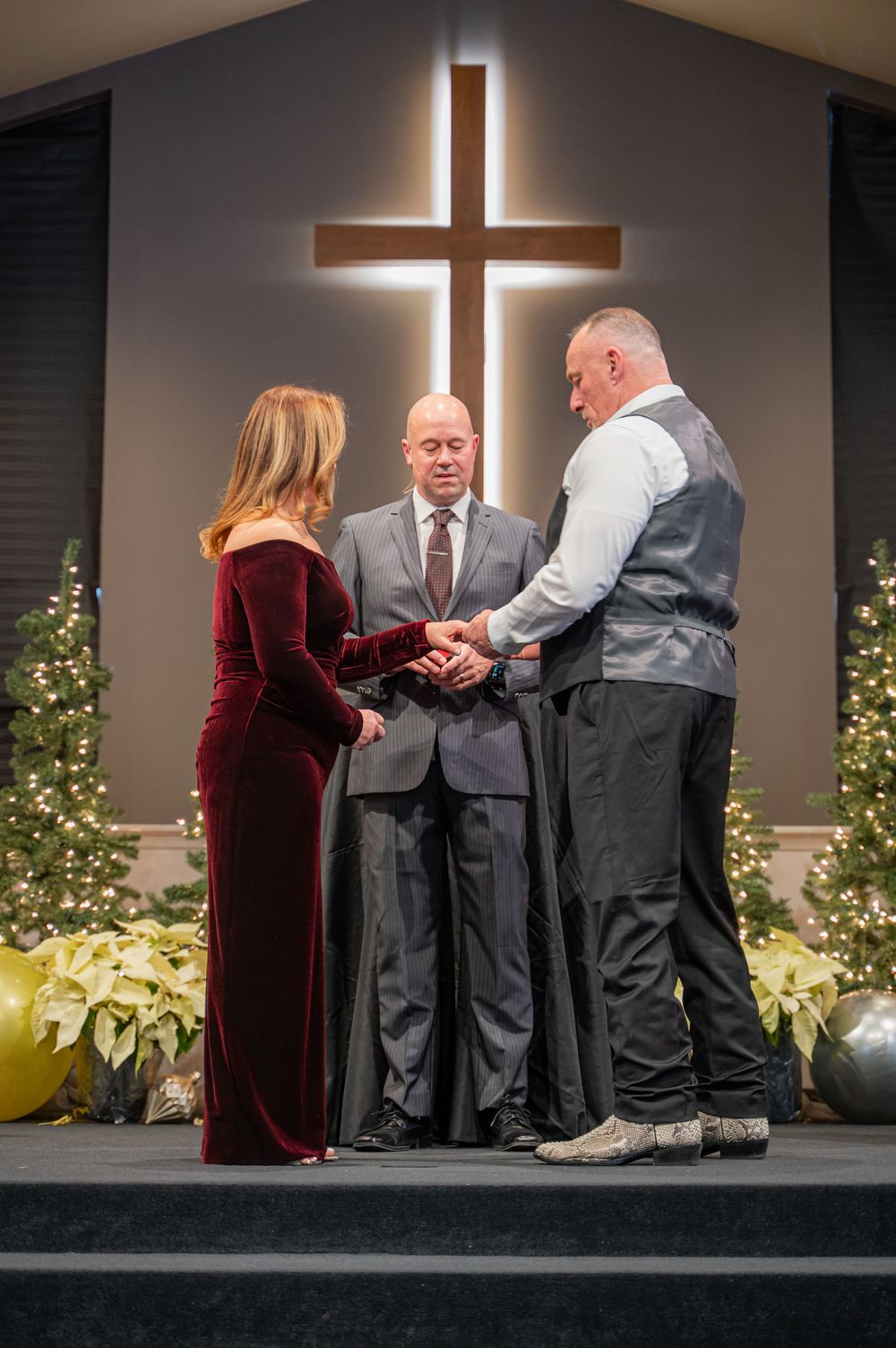 Multiple people kneeling together on a church stage with illuminated crosses and Christmas decorations in the background.