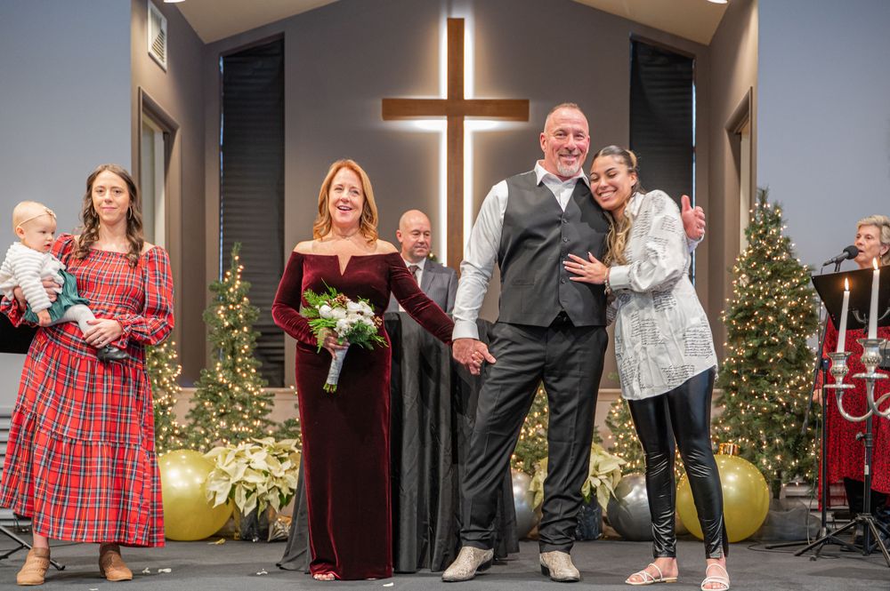 A group of people gather during a holiday event in front of an illuminated cross at a church.