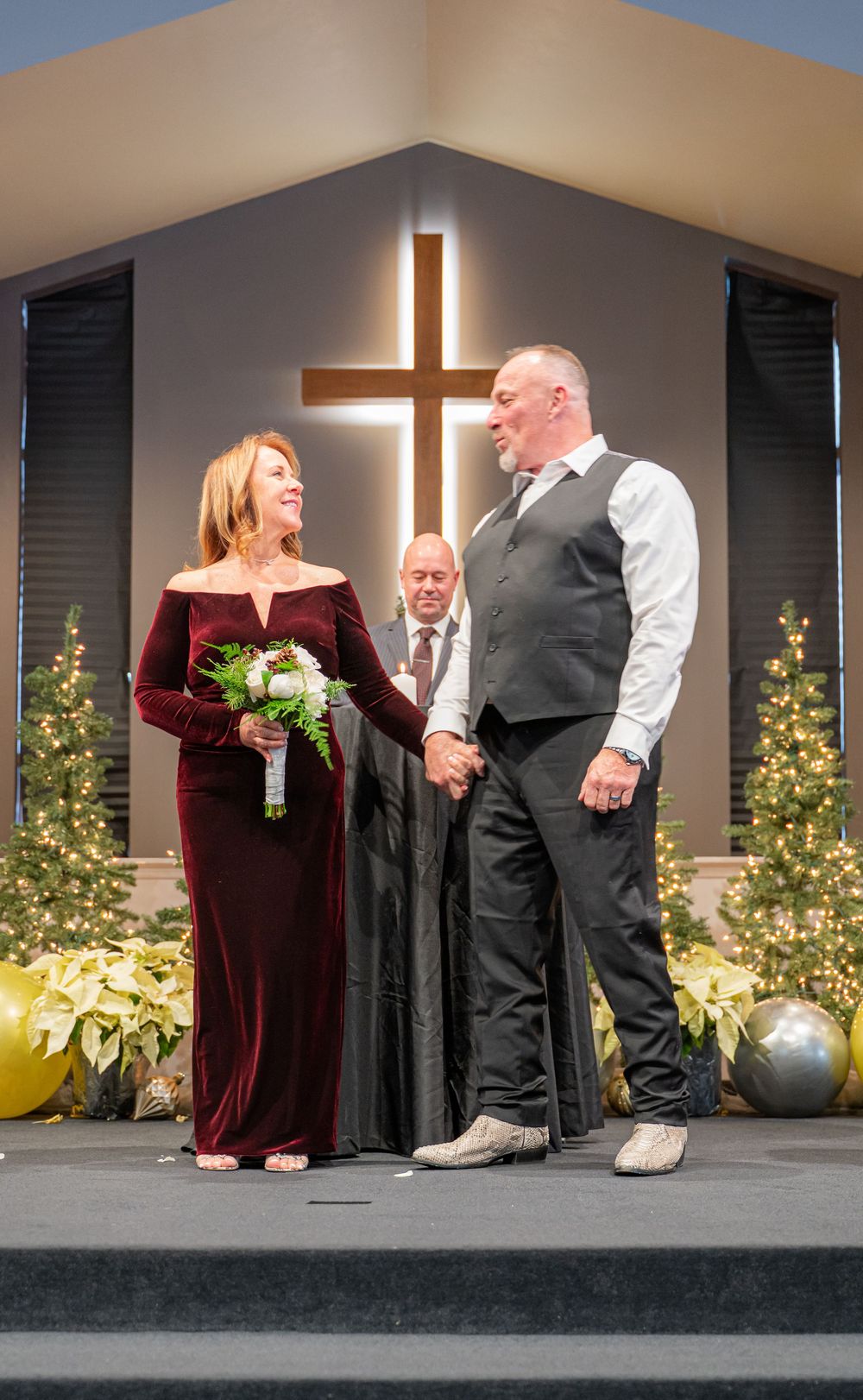 A wedding ceremony takes place at a church altar with a large illuminated cross and holiday decorations.