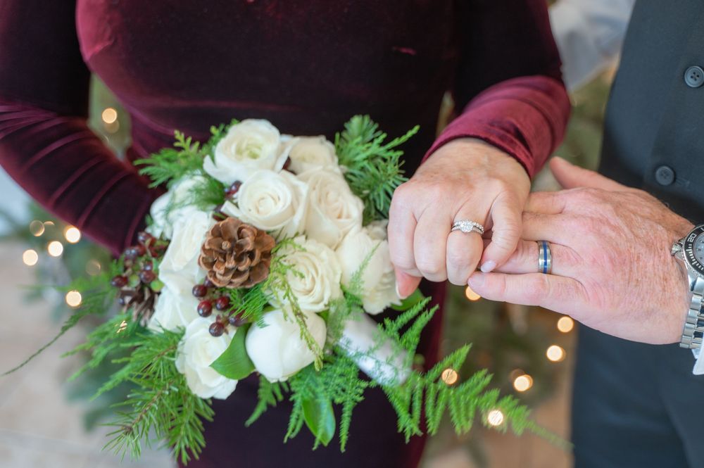 Wedding floral detail photography showing delicate ivory roses and greenery bouquets held by burgundy-clad figures.