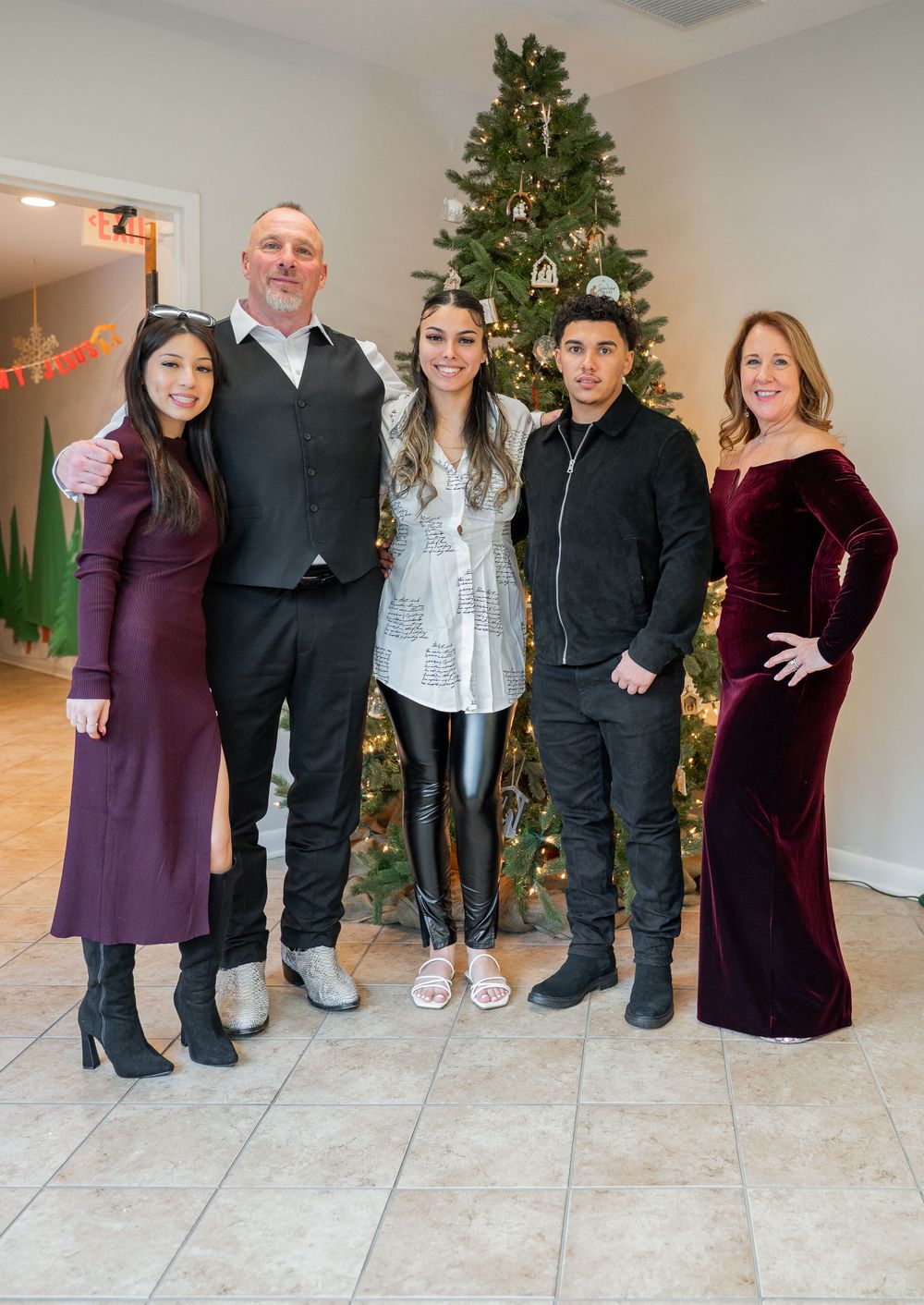 A group of people pose together in front of a decorated Christmas tree in a home interior setting.