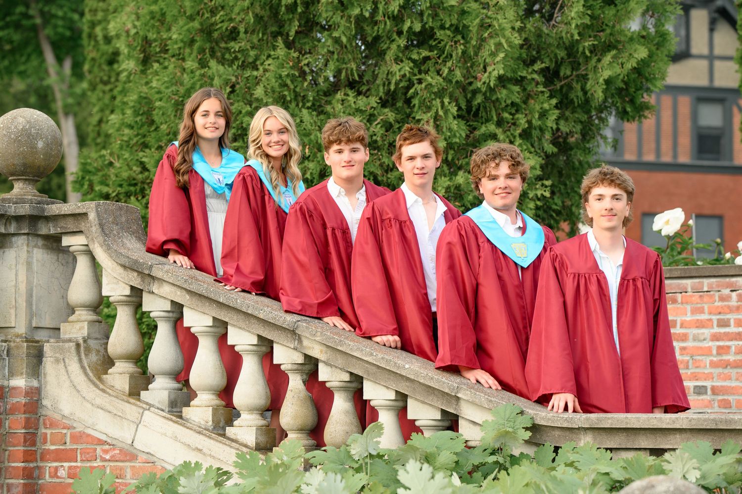 Group of graduates in red gowns posed on outdoor brick stairs for commencement photos.
