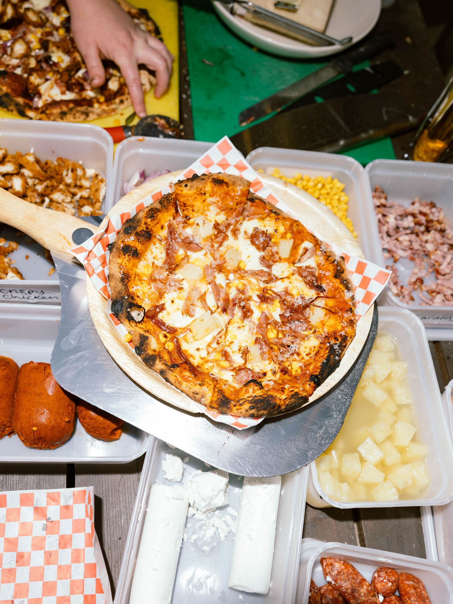 A gourmet pizza topped with melted cheese and toppings sits on a tray surrounded by various ingredient containers.