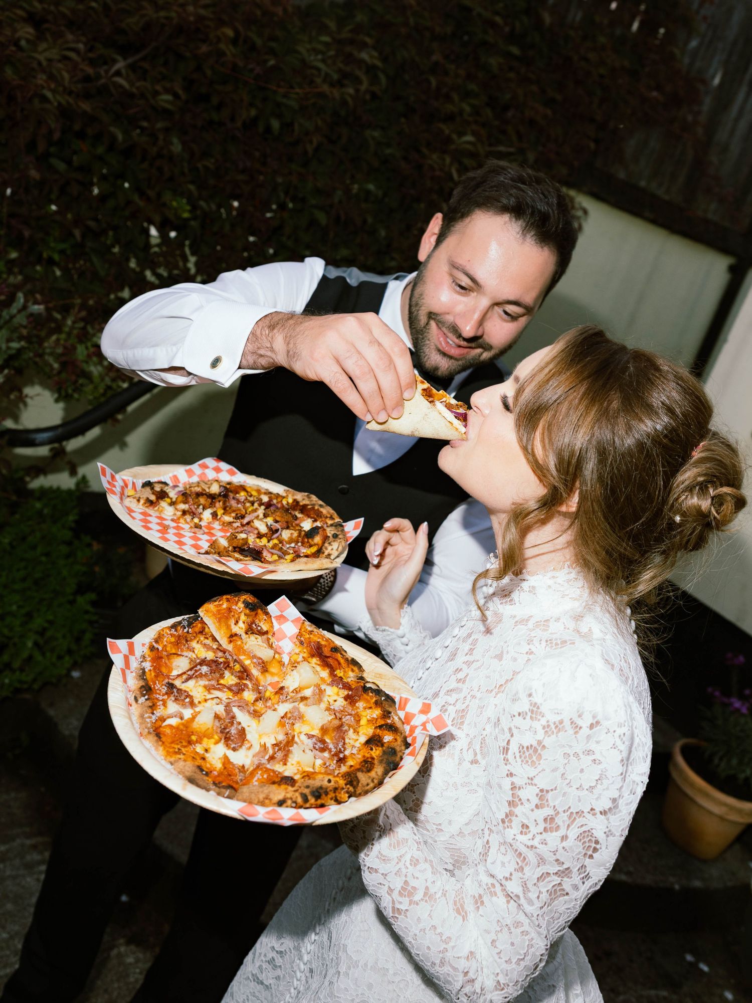 A couple shares pizza while dressed in formal attire during an outdoor evening celebration.