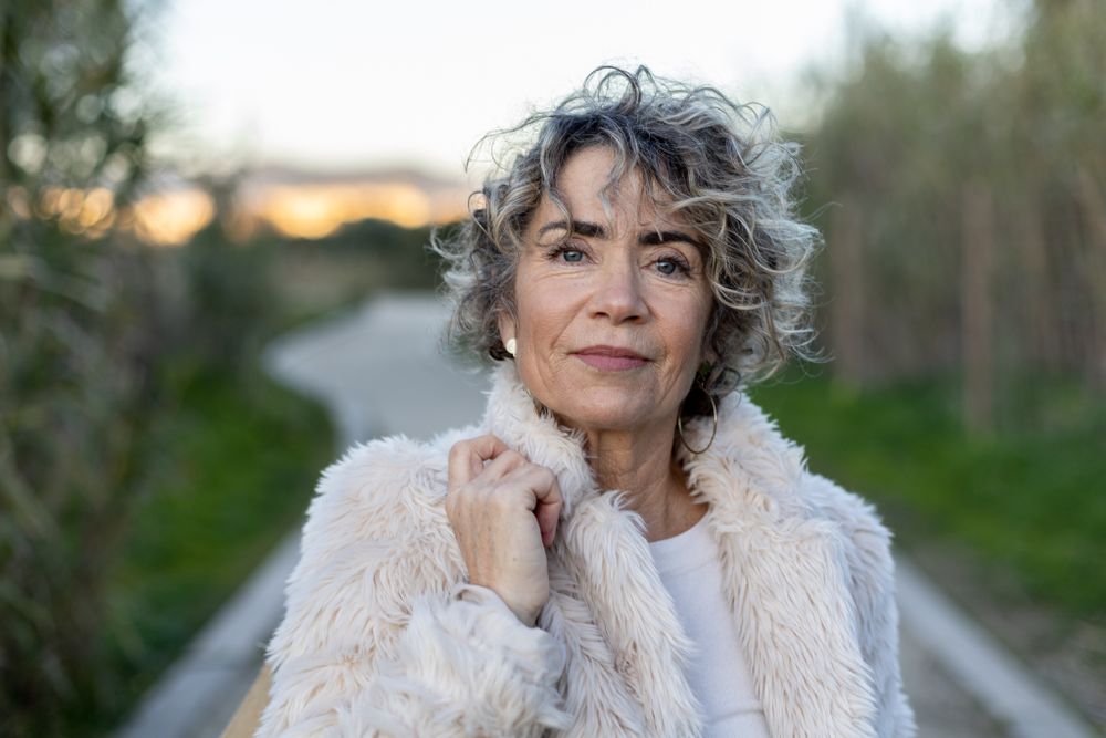 Portrait of a short curly-haired woman with her furry jacket looking at the camera.