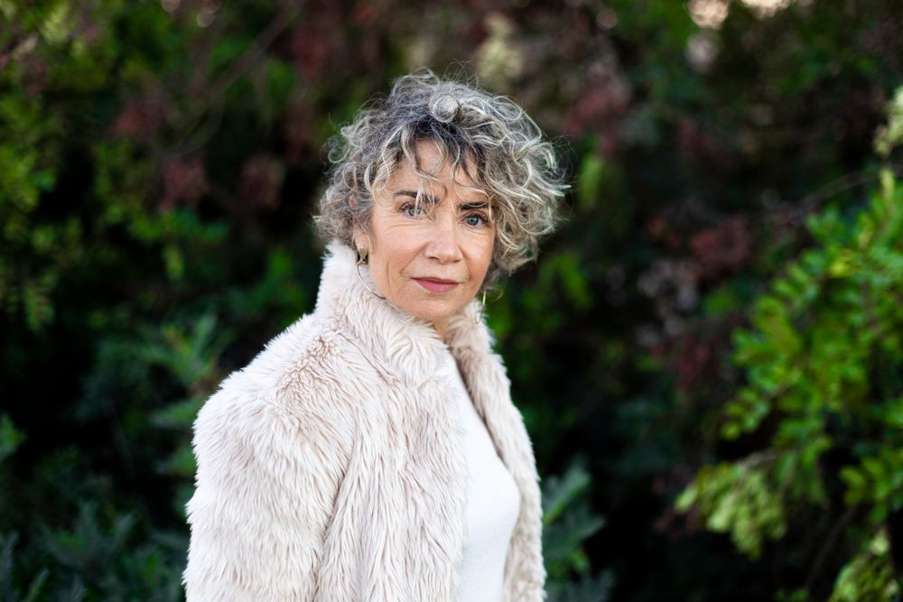 Portrait of a short curly-haired woman with her furry jacket looking at the camera.