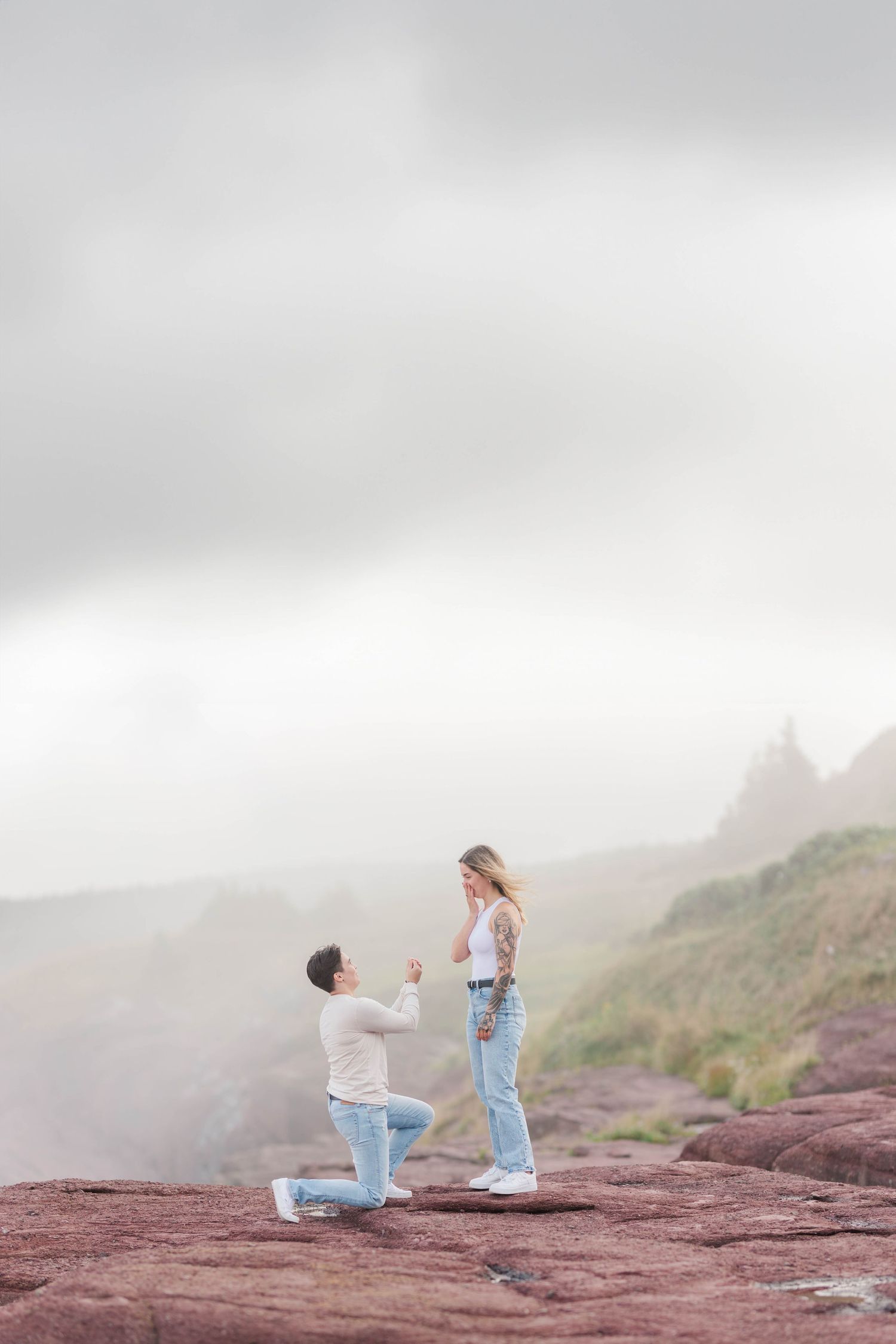Marriage proposal scene unfolding on dramatic red coastal cliffs of Flatrock, Newfoundland.