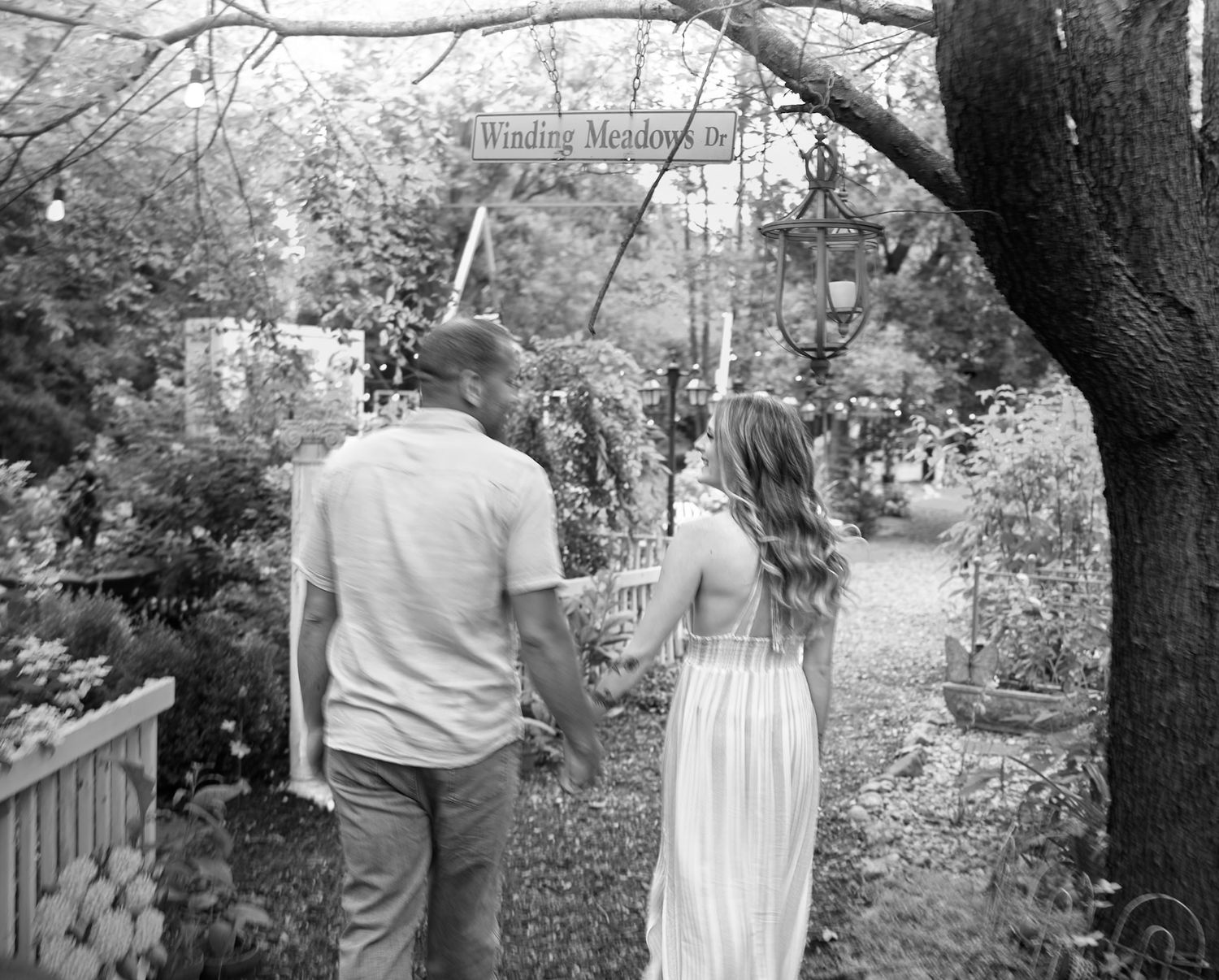 Black and white photo of a couple walking together on a garden path surrounded by trees.