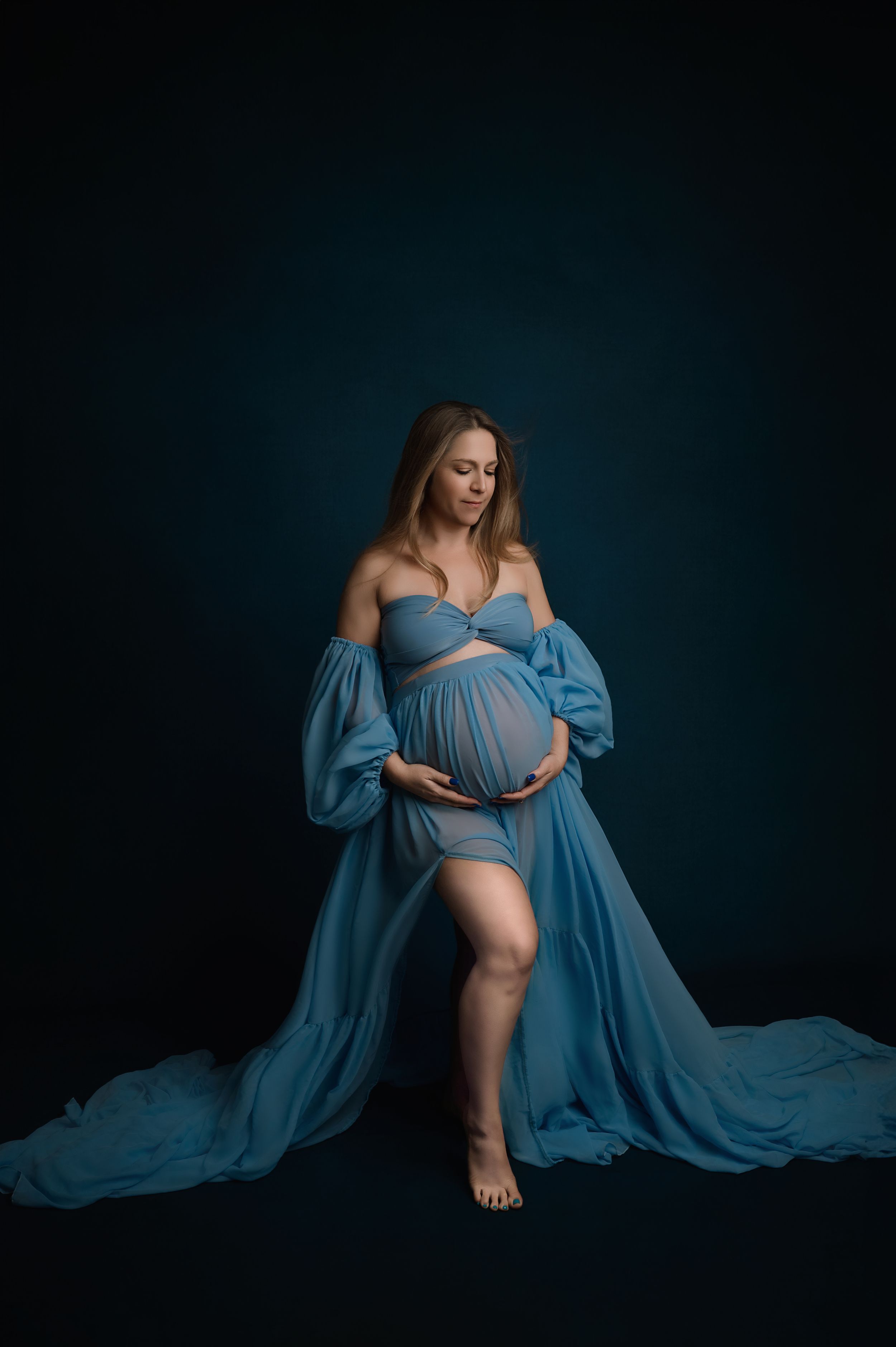A series of four moody maternity portraits with a woman in blue flowing fabric against a dark background.
