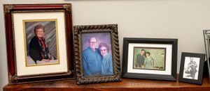Collection of family portraits in various frames displayed on wooden surface showing casual and formal photographs.