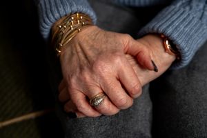 Close up shot of hands with stacked bracelets and rings resting on dark fabric.