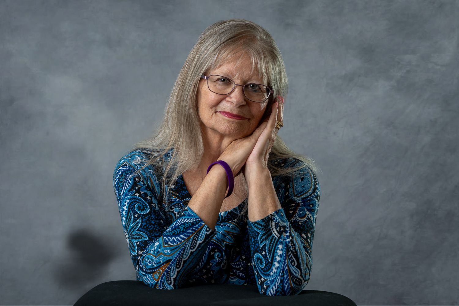 Professional studio portraits showing a person wearing glasses and a blue floral print top against a gray background.