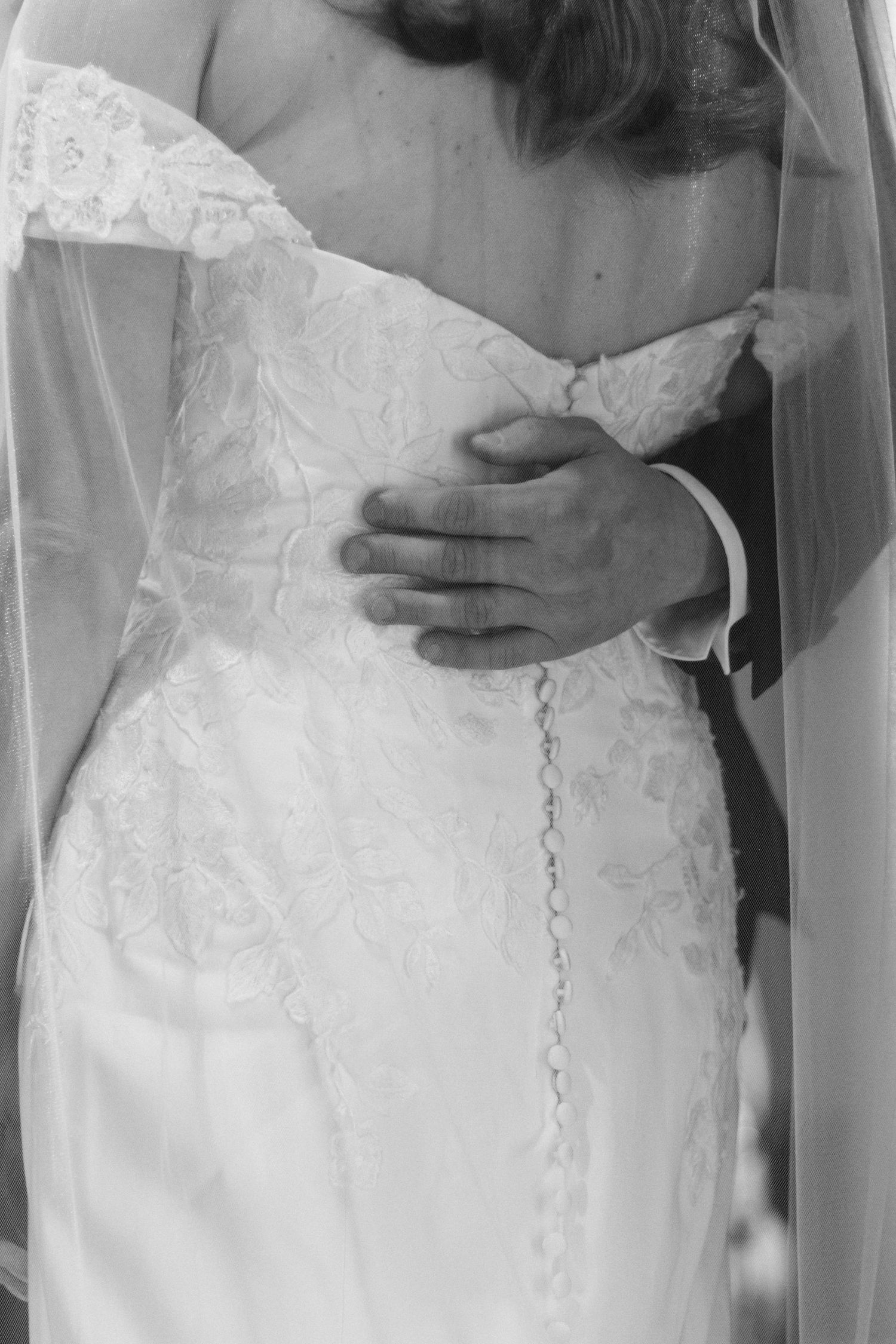 Close up of Groom's hand resting on the Brides back, white dress with floral lace pattern captured in black and white