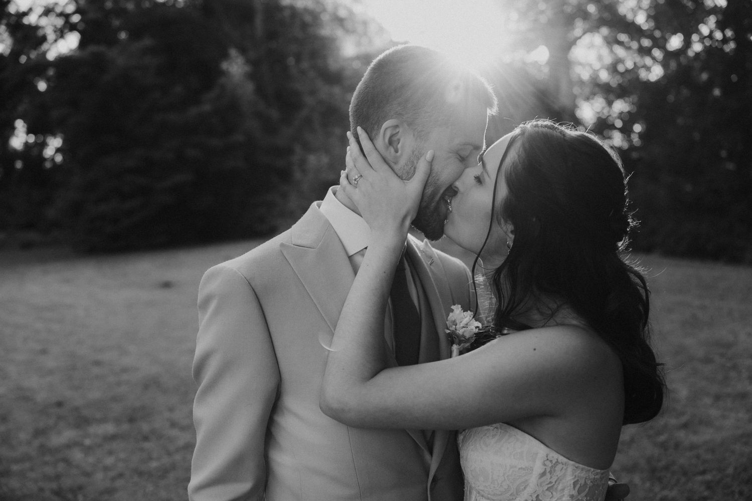 A romantic black and white wedding photograph showing a tender embrace in a natural outdoor setting.