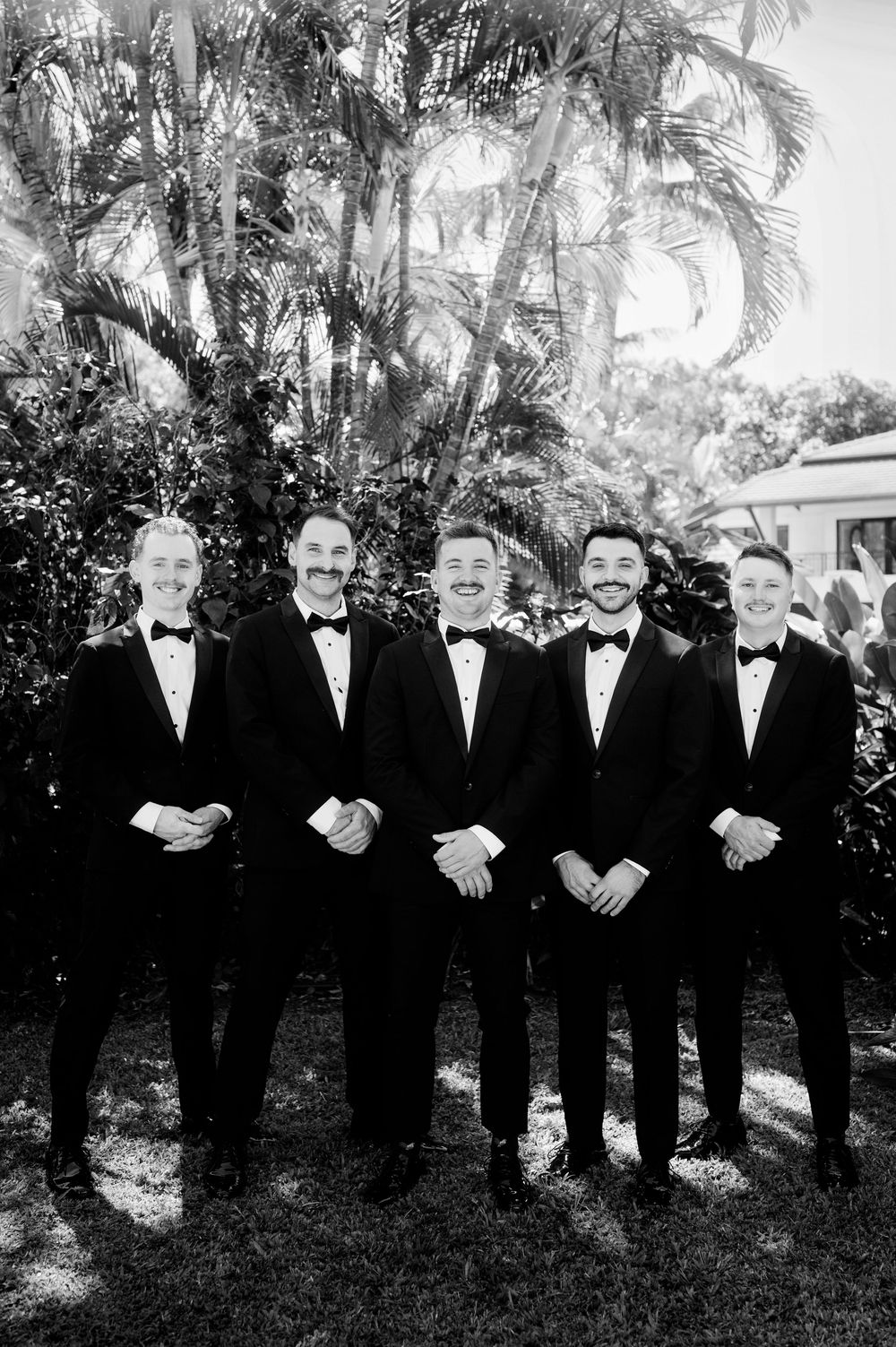 Black and white portrait of groomsmen standing together in a tropical garden setting.