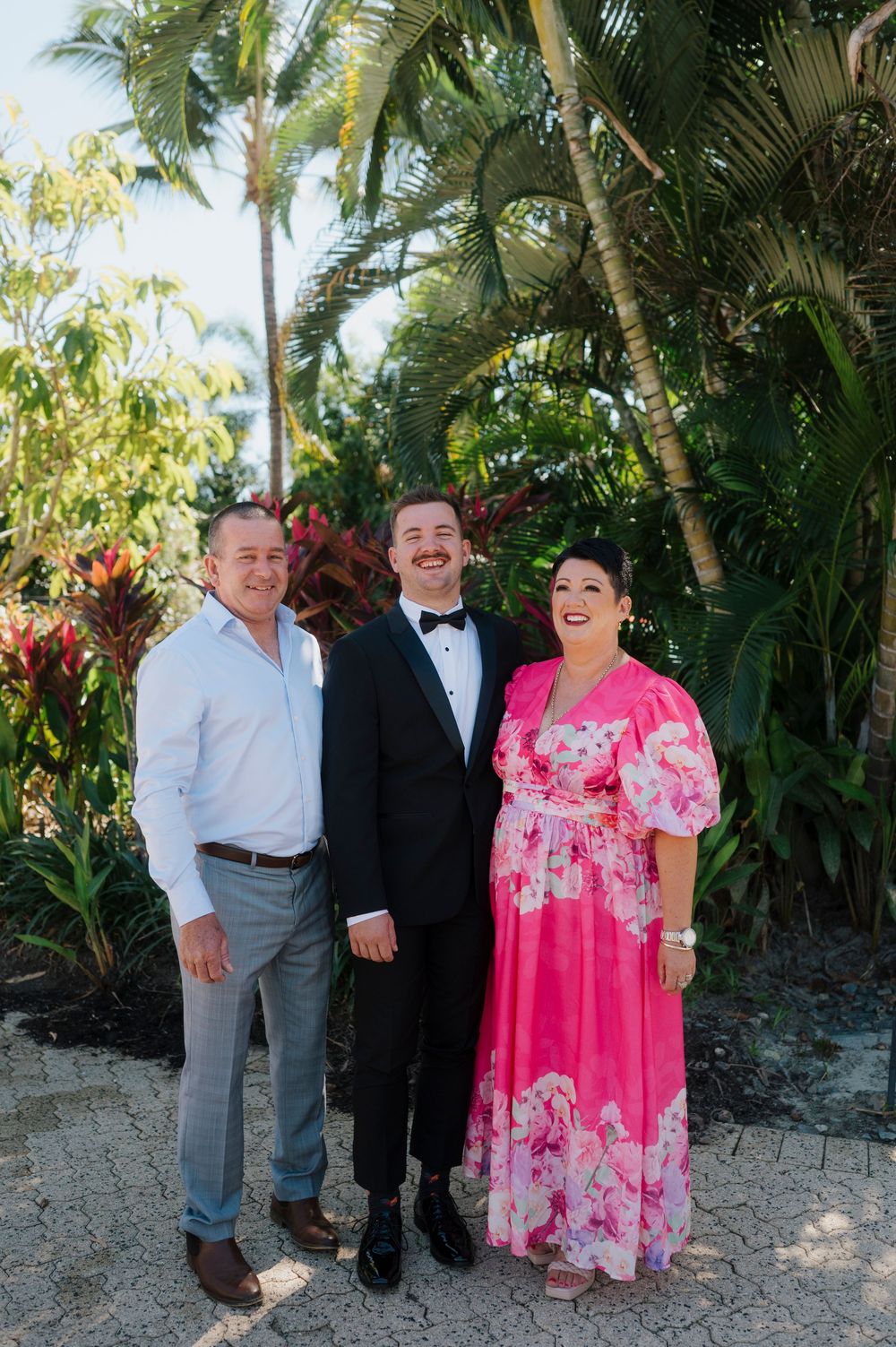 Three guests share a candid moment against a lush tropical backdrop with palm trees.