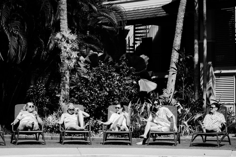 Black and white photo of guests relaxing in row of lounge chairs at tropical resort.