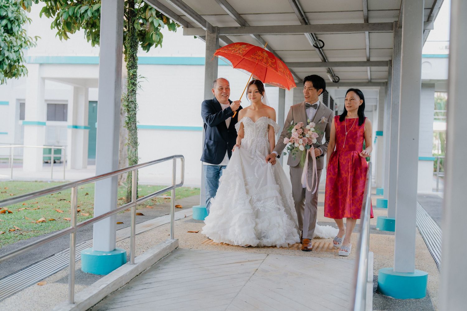 Wedding party celebrating in a covered walkway with natural lighting and orange umbrellas.