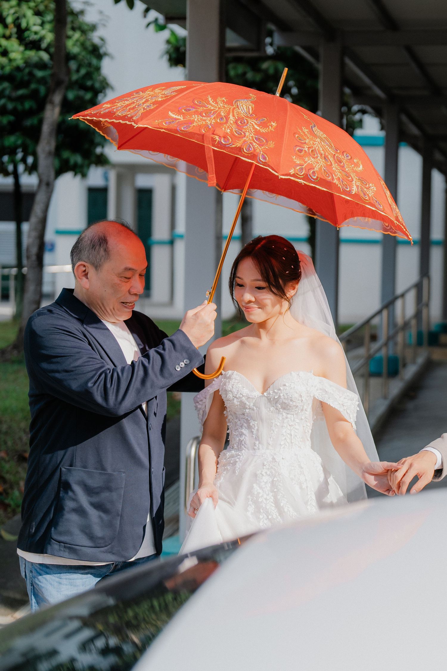 Couple under ornate red umbrella during outdoor wedding ceremony.