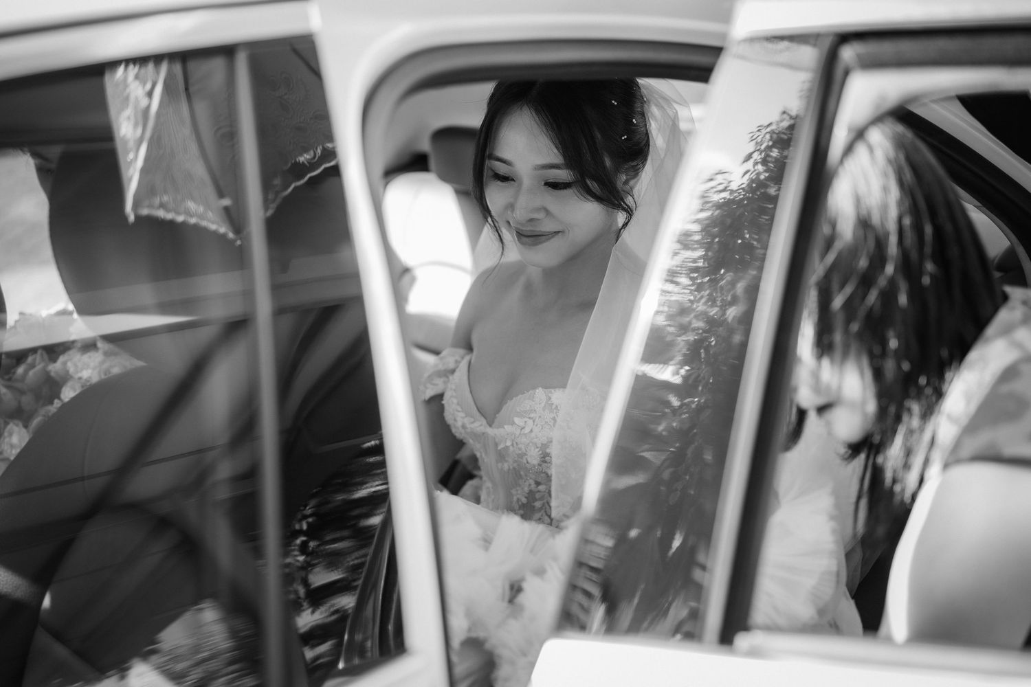 Black and white photo of someone in wedding attire sitting inside a classic car.