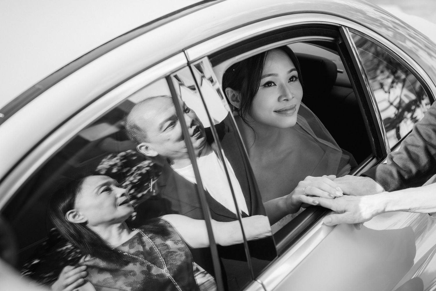 Bride in white wedding dress sitting in car captured in black and white photography.