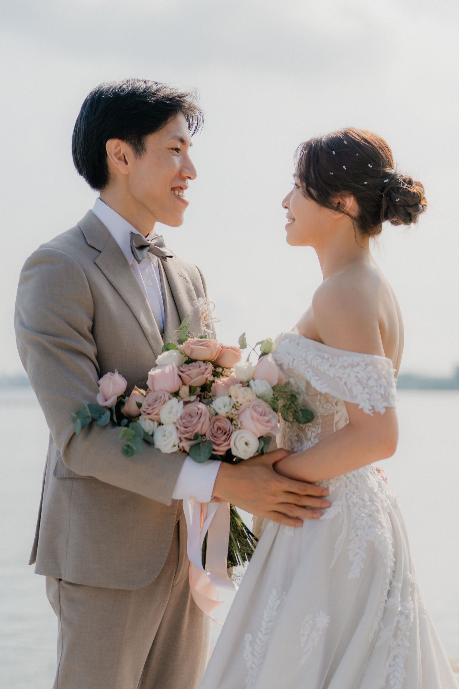 Romantic outdoor wedding photo with couple sharing a joyful moment and holding blush pink rose bouquet.