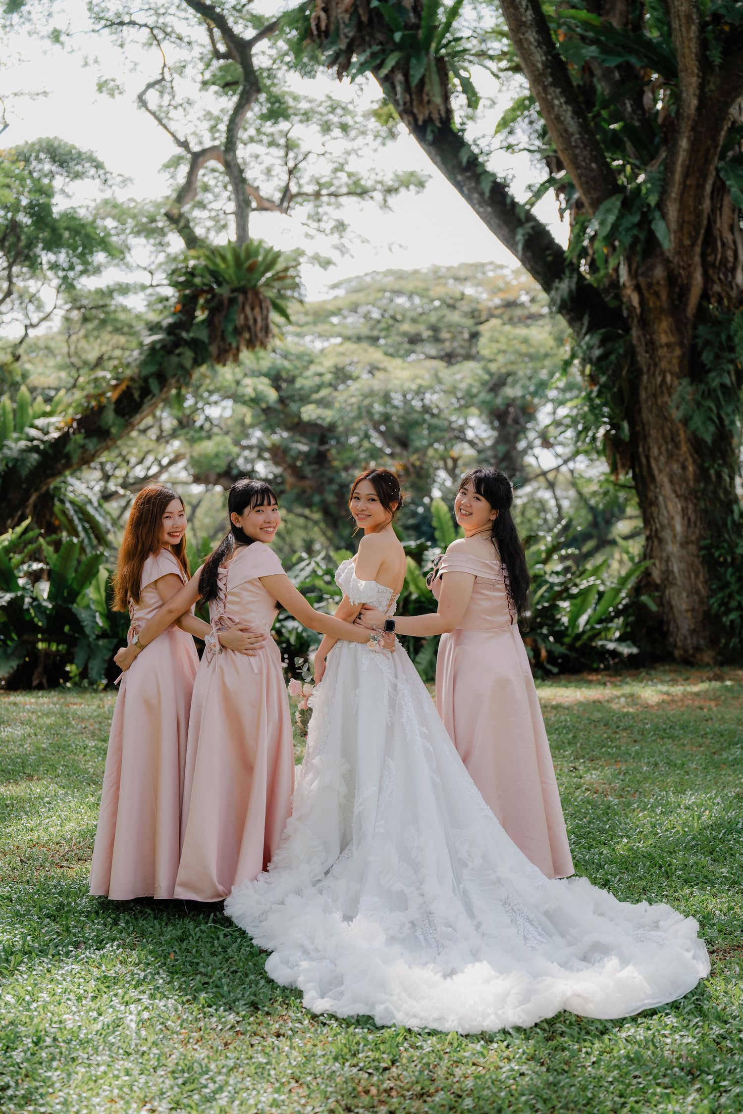 Wedding party in pink dresses and white gown pose together in a lush garden setting.