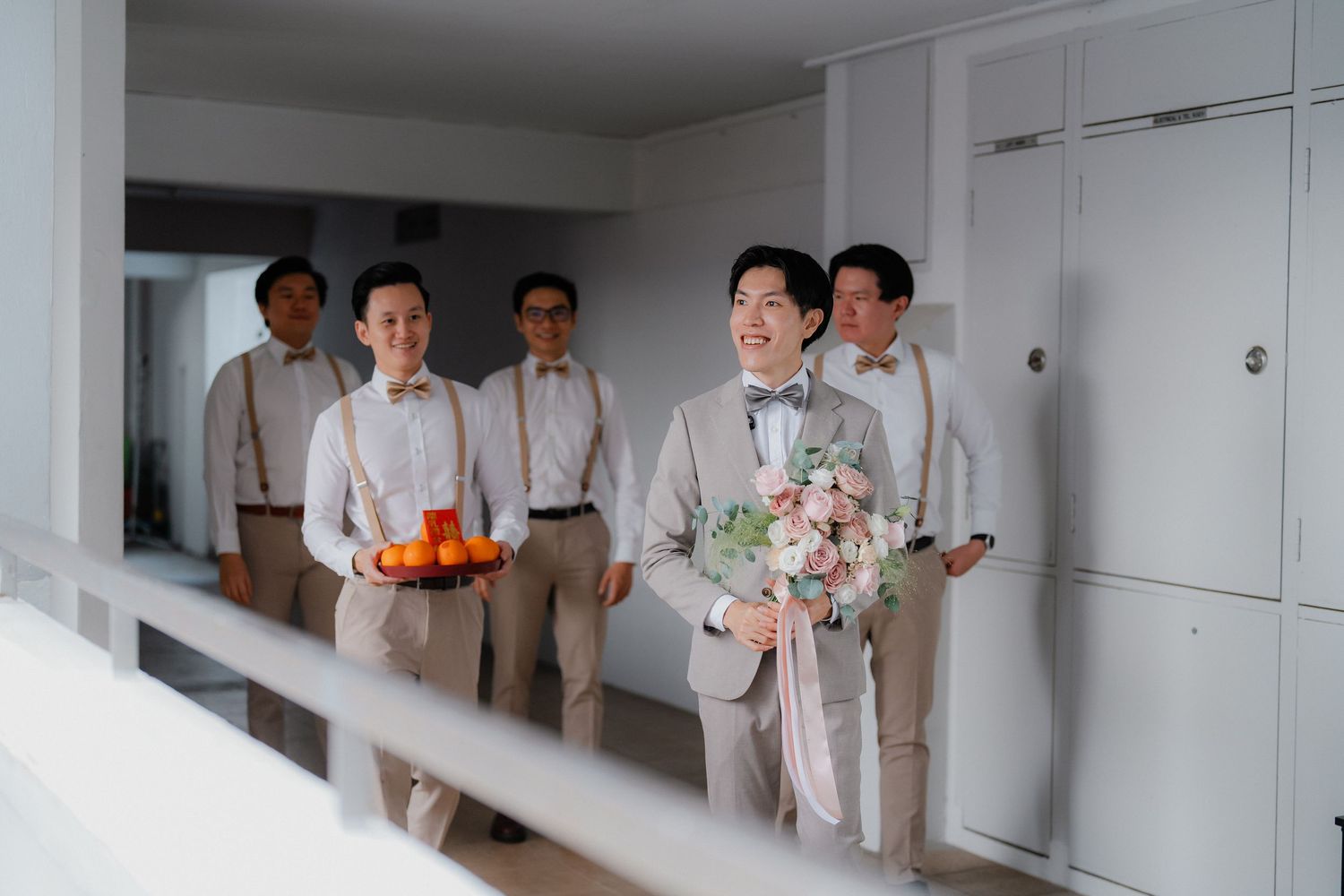 Wedding party groomsmen in beige suits walking down a hallway with flowers and boutonnieres.