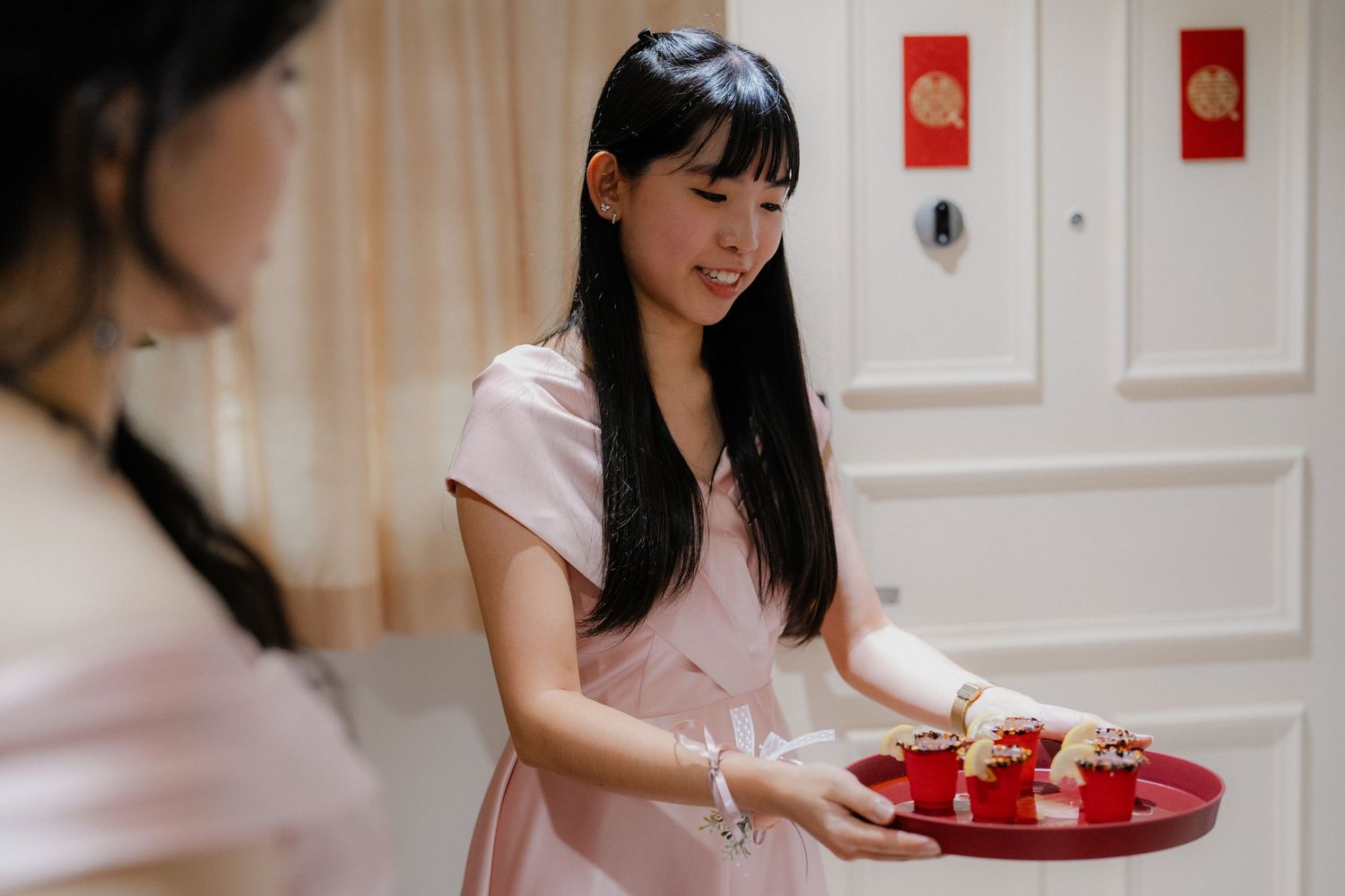 Person in pink dress serves traditional tea ceremony items on red tray.