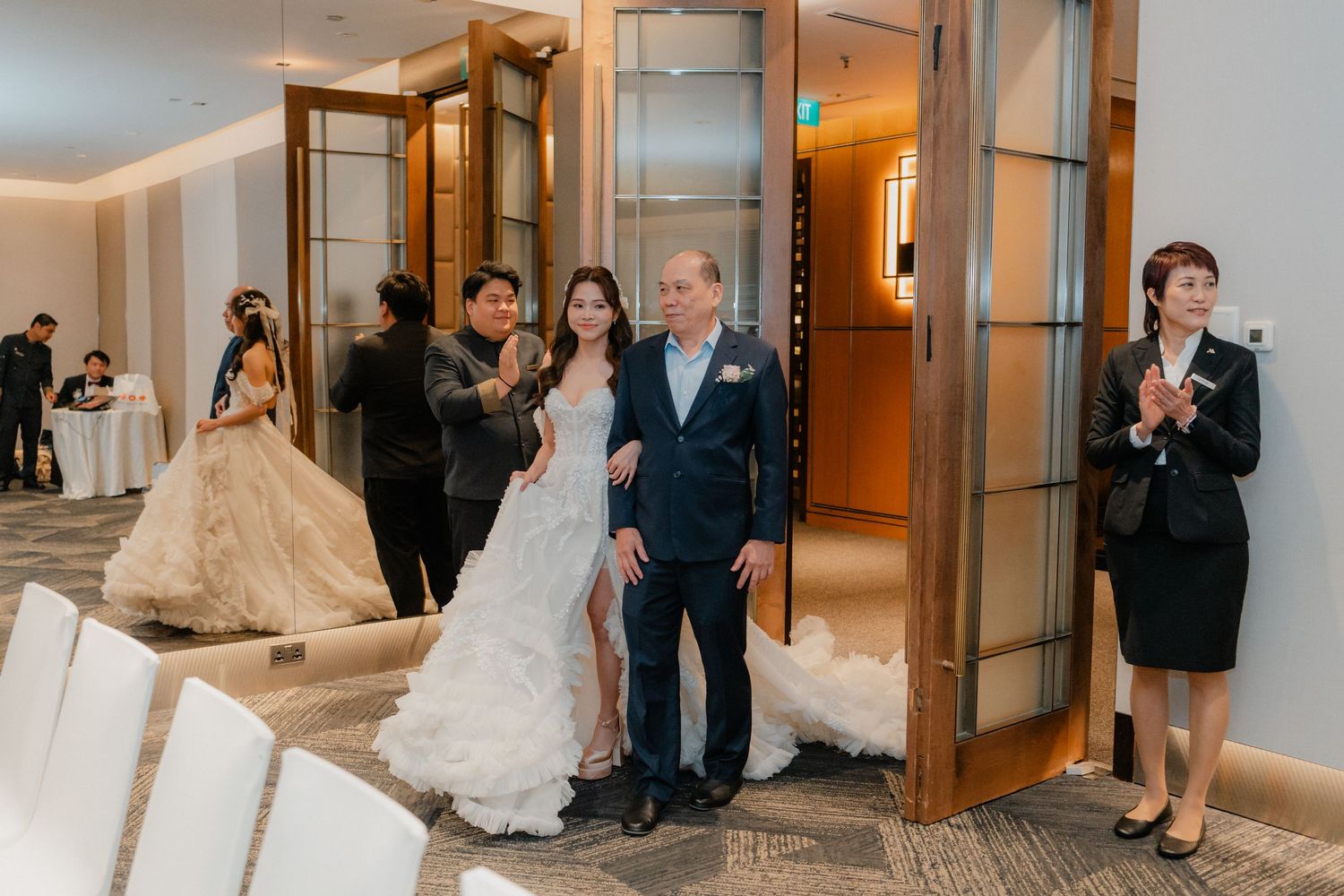 Wedding party members walk through an elegant hotel hallway lined with glass doors.