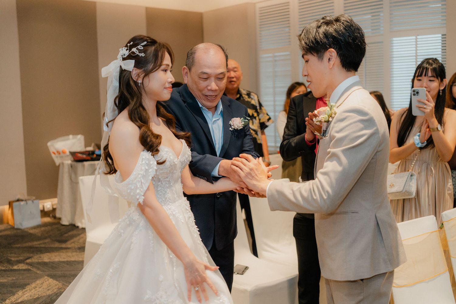 A wedding ceremony takes place indoors with the couple and officiant exchanging vows in a bright room.