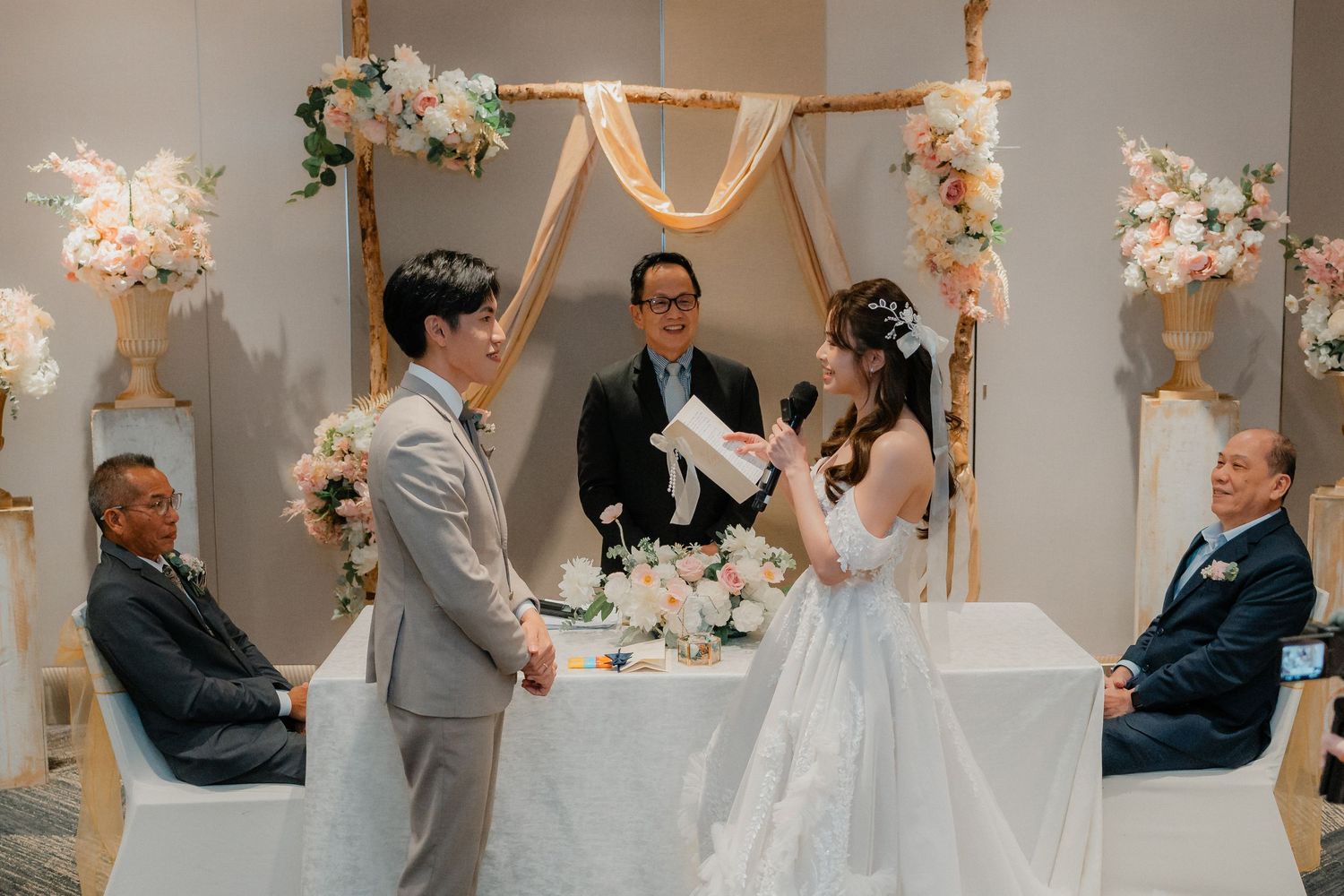 An intimate wedding ceremony taking place under a decorated arch with floral arrangements.