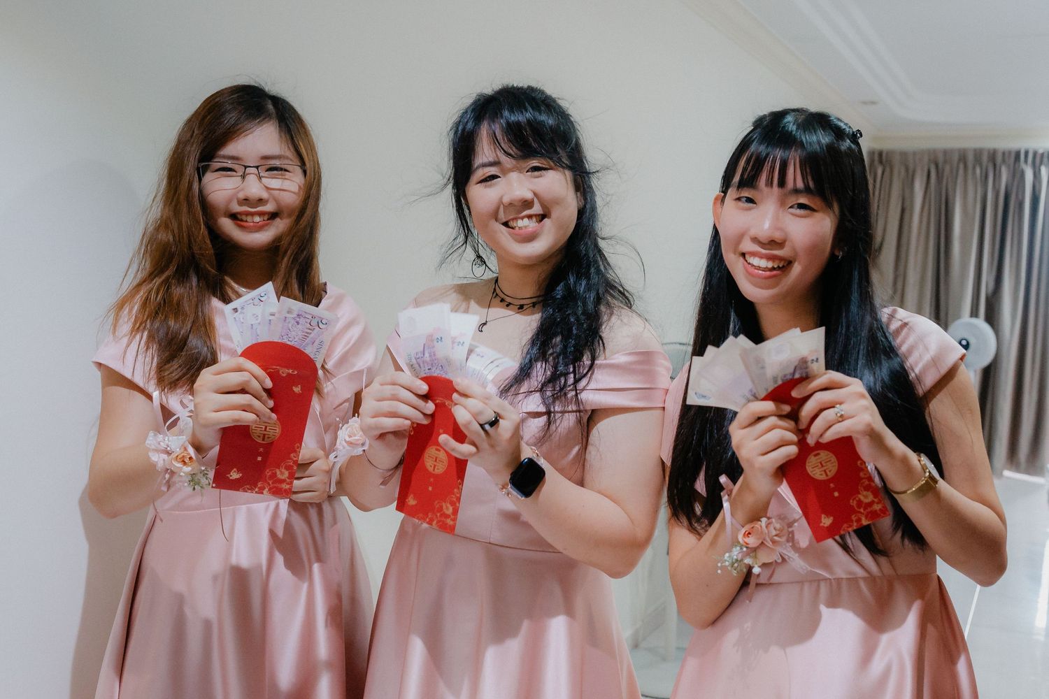 Bridesmaids in pink dresses hold red envelopes during wedding celebrations.