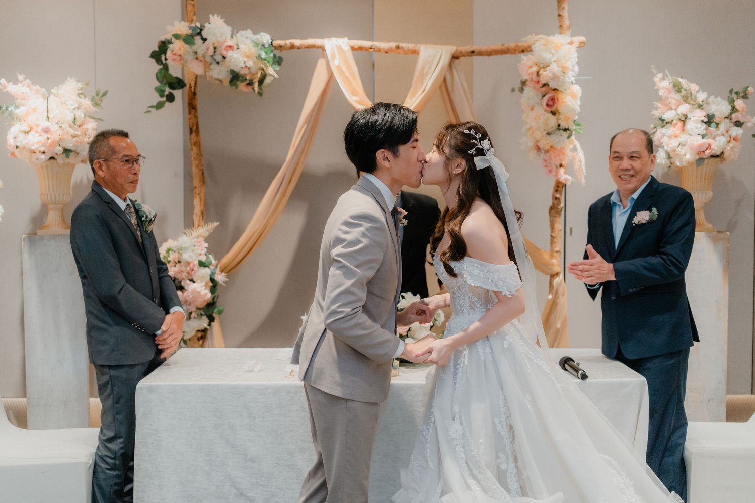 Wedding ceremony in an elegantly decorated indoor venue with white and pink floral arrangements.