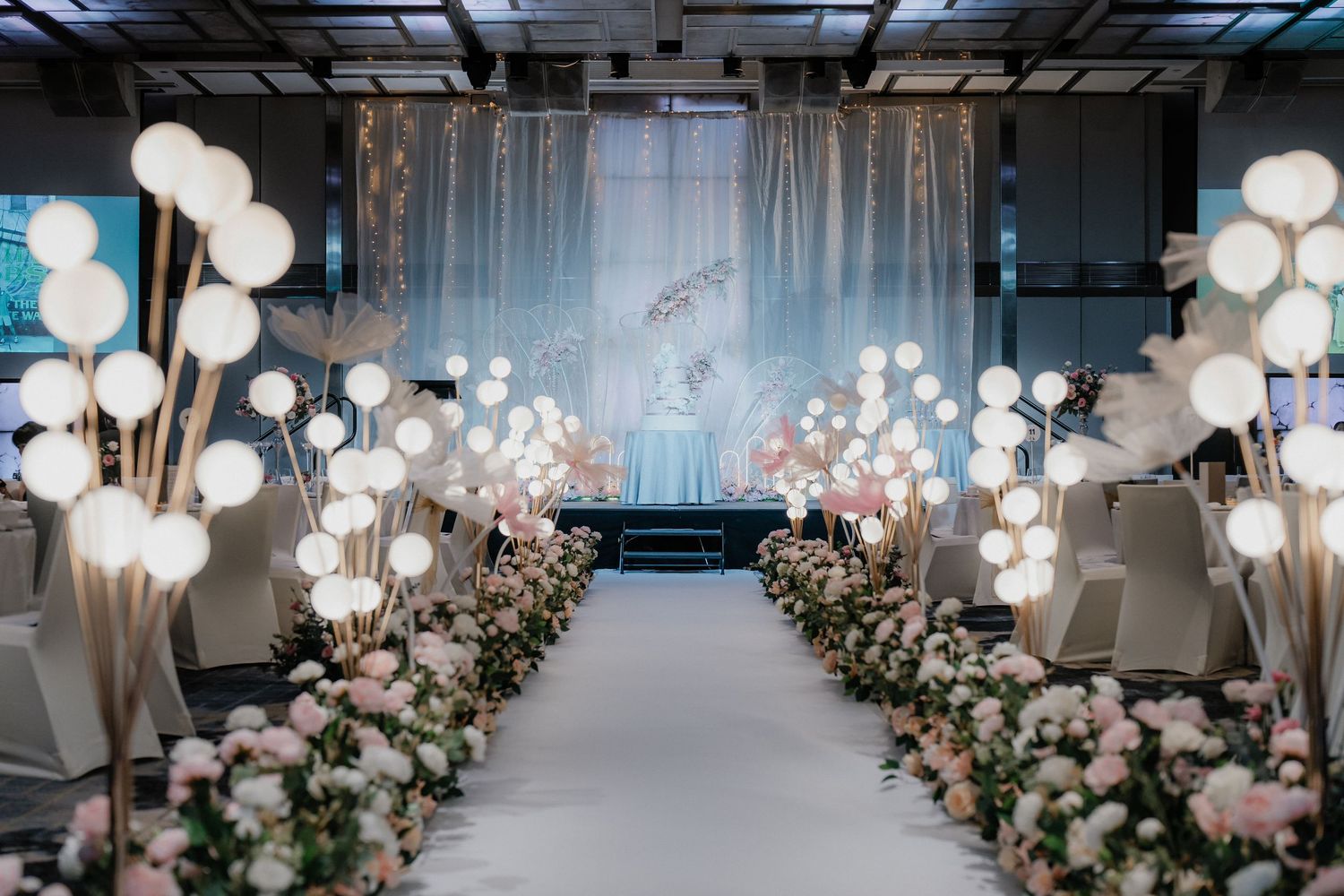 Modern wedding ceremony aisle decorated with hanging glass orbs and floral arrangements.