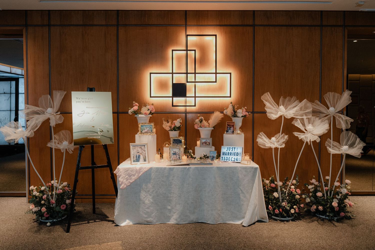 Wedding dessert table with geometric wall art and decorative white paper flowers on stands.