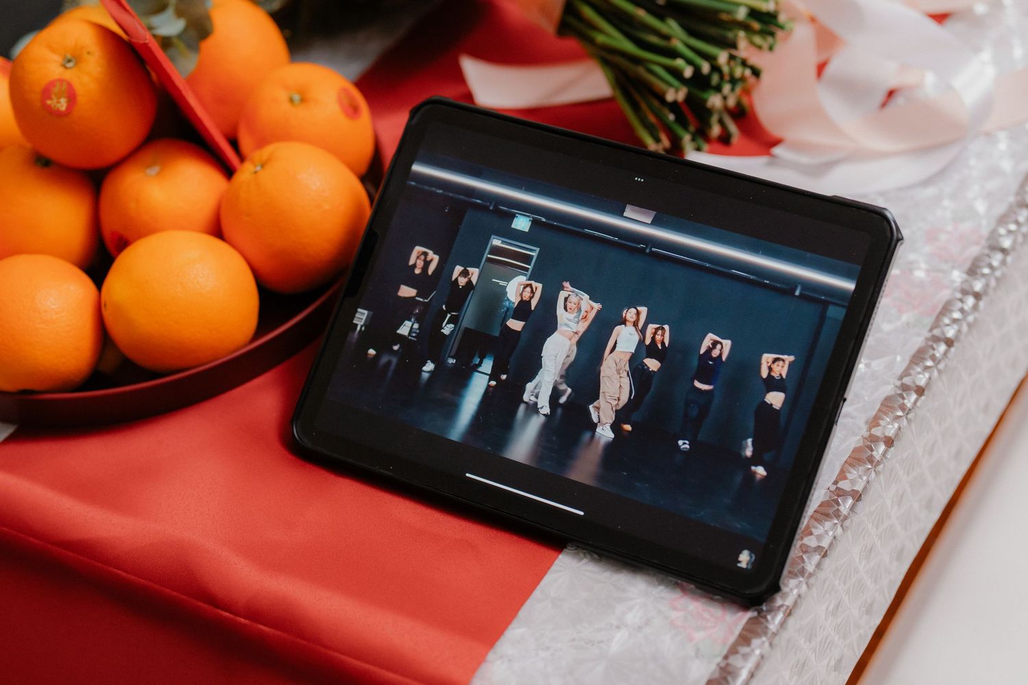 Tablet displays wedding party photos next to bowl of oranges on red tablecloth.