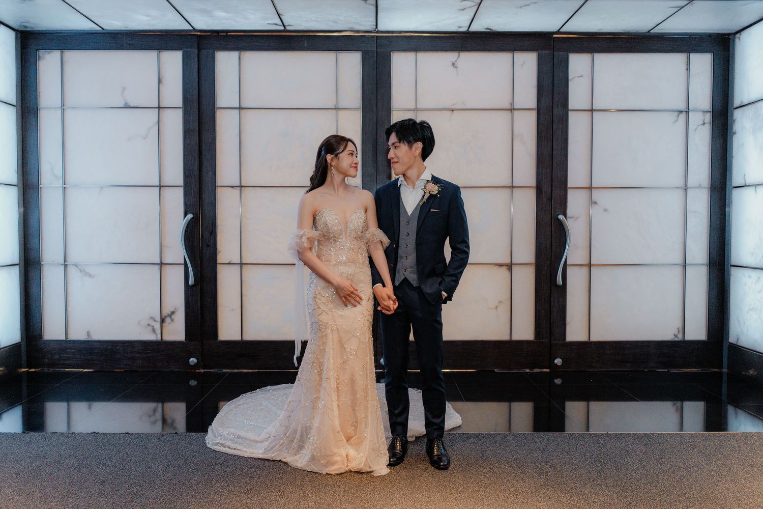 Bride and groom share an intimate moment in an elegant white corridor.