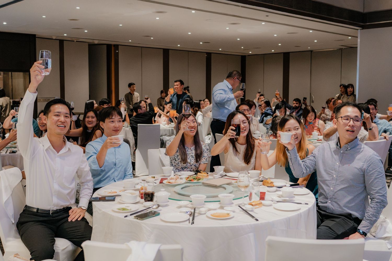 Large wedding reception hall filled with guests seated at round tables during celebration.