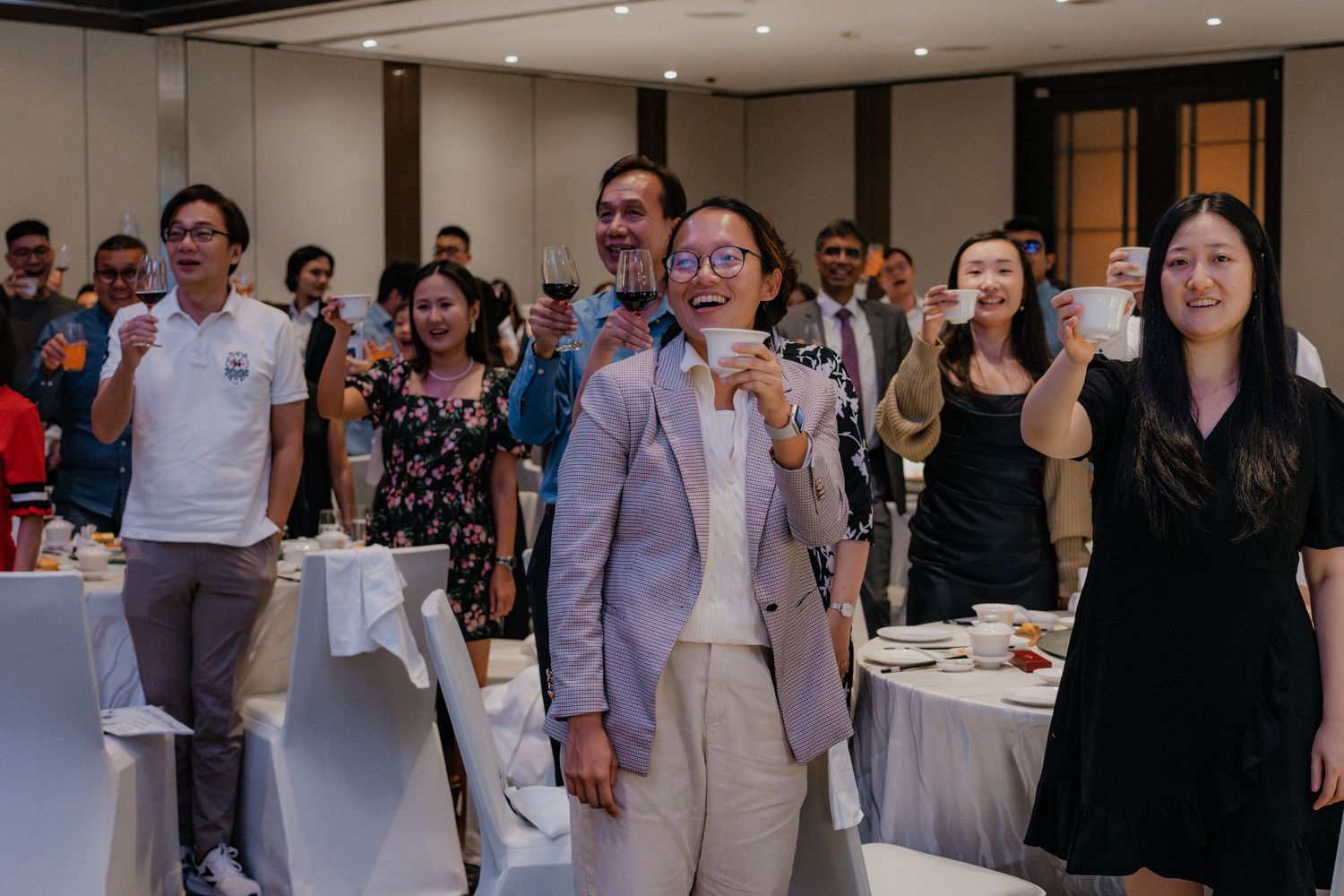 Wedding guests stand and smile during a celebration in an elegantly decorated banquet hall.