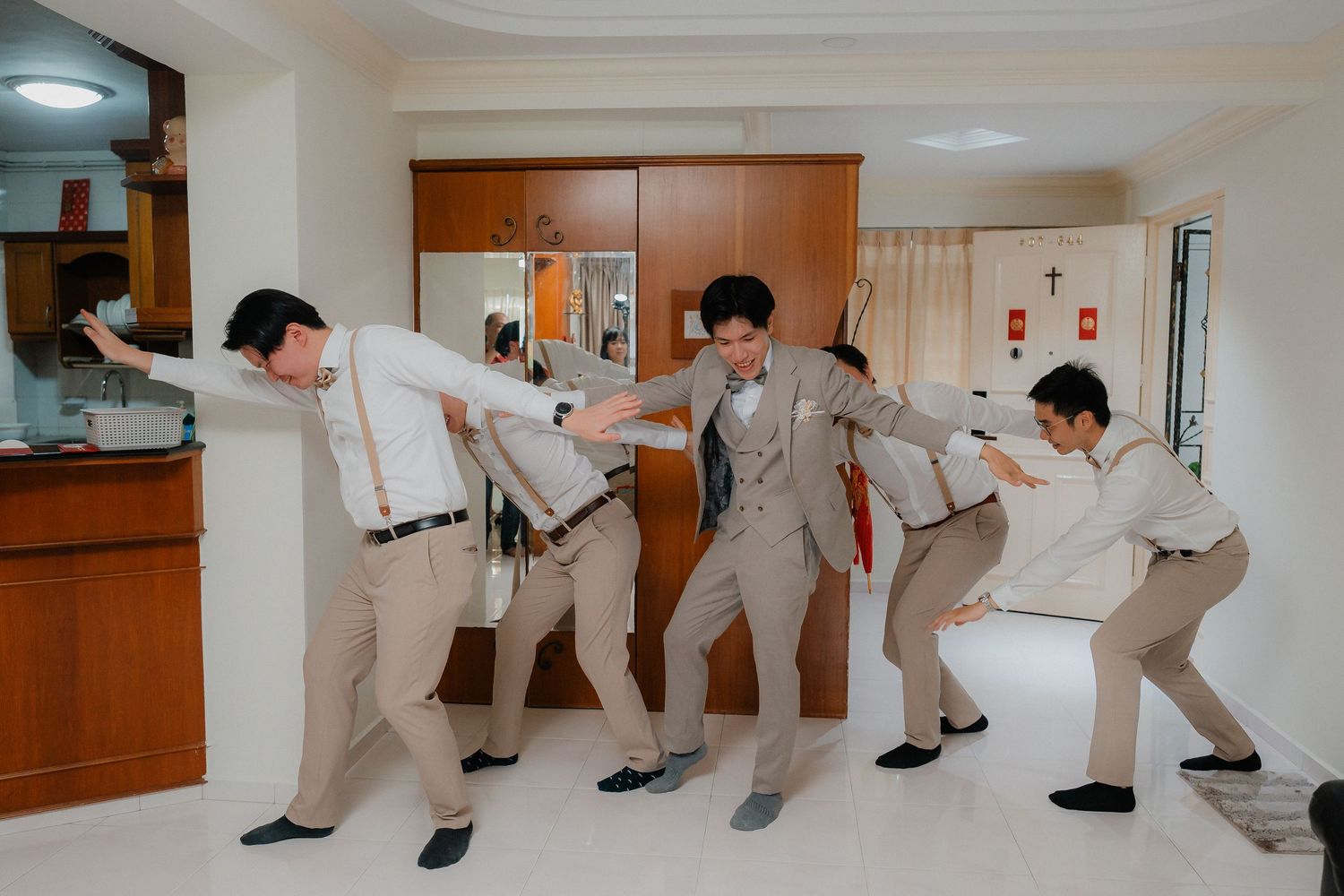 Groomsmen in beige suits striking funny poses in an indoor venue.