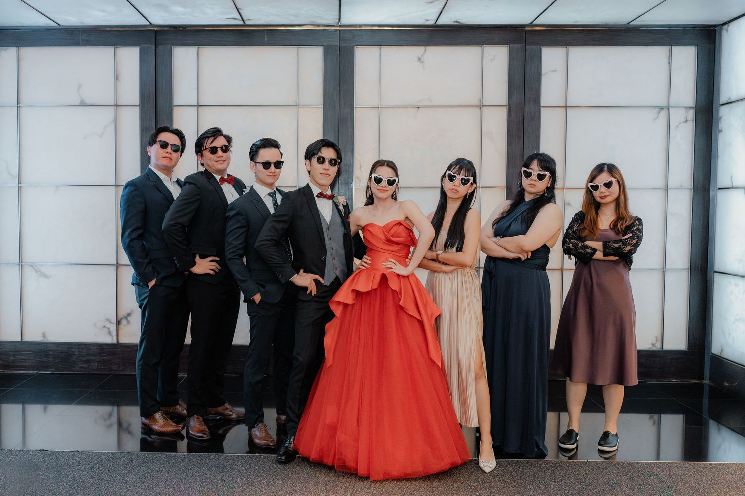 Wedding party poses together in formal attire featuring a red gown and dark suits.