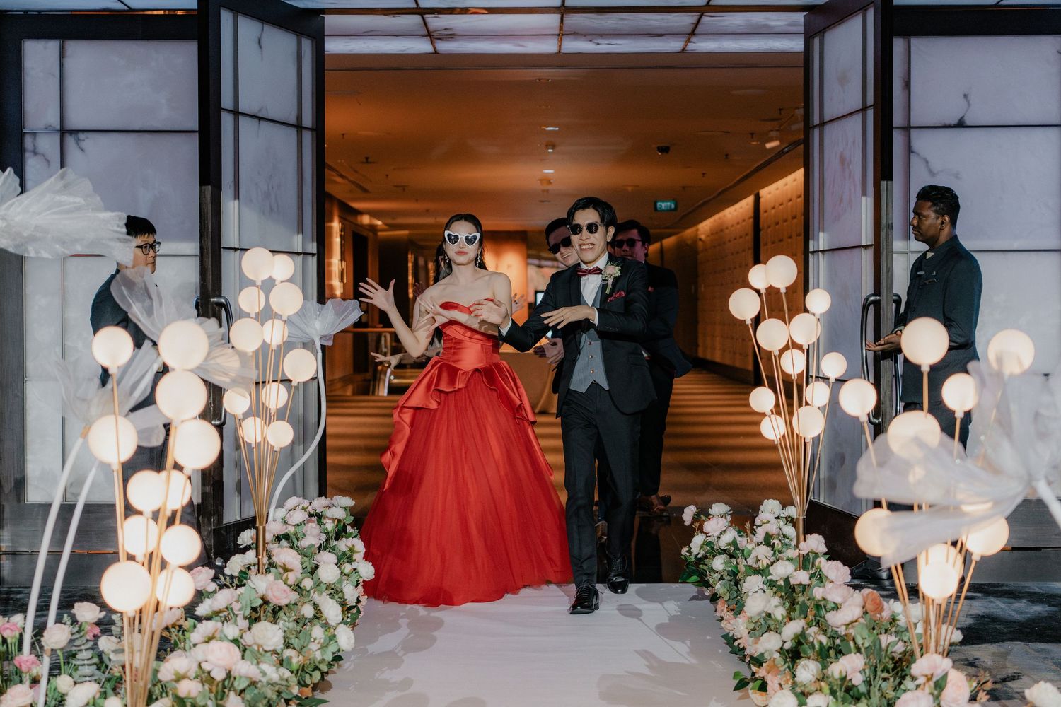 Couple making grand entrance through hallway decorated with glowing lanterns and floral arrangements.