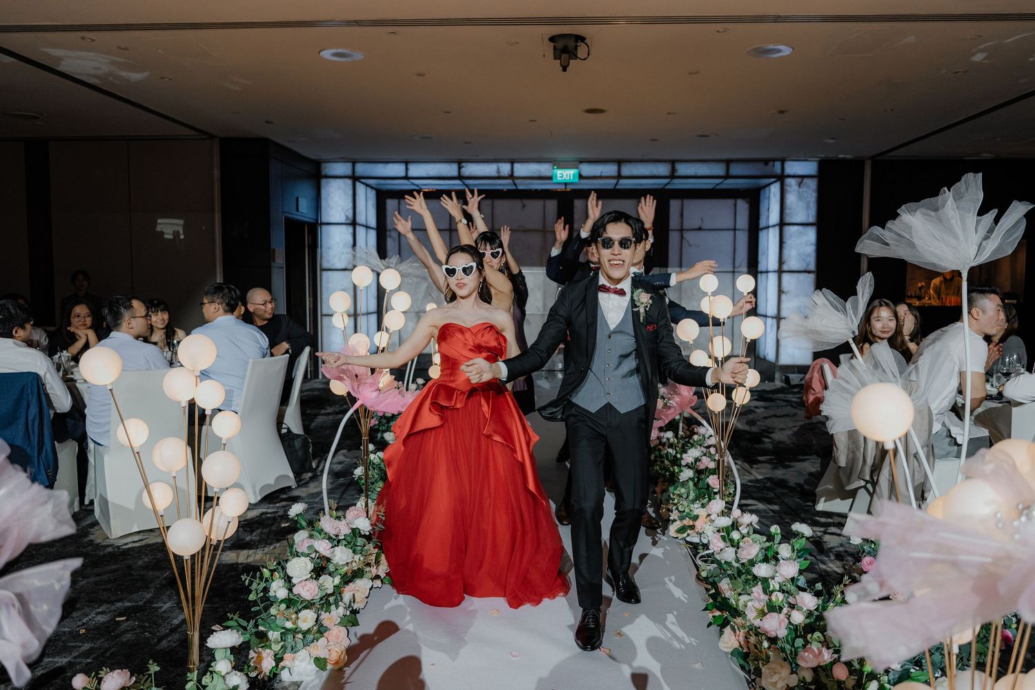 A couple celebrates their wedding ceremony walking down an aisle decorated with flowers and white pampas grass stems.