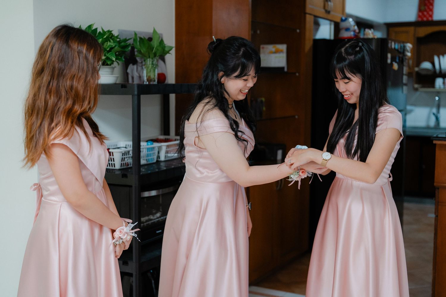 Three bridesmaids in pink dresses share a moment together indoors.