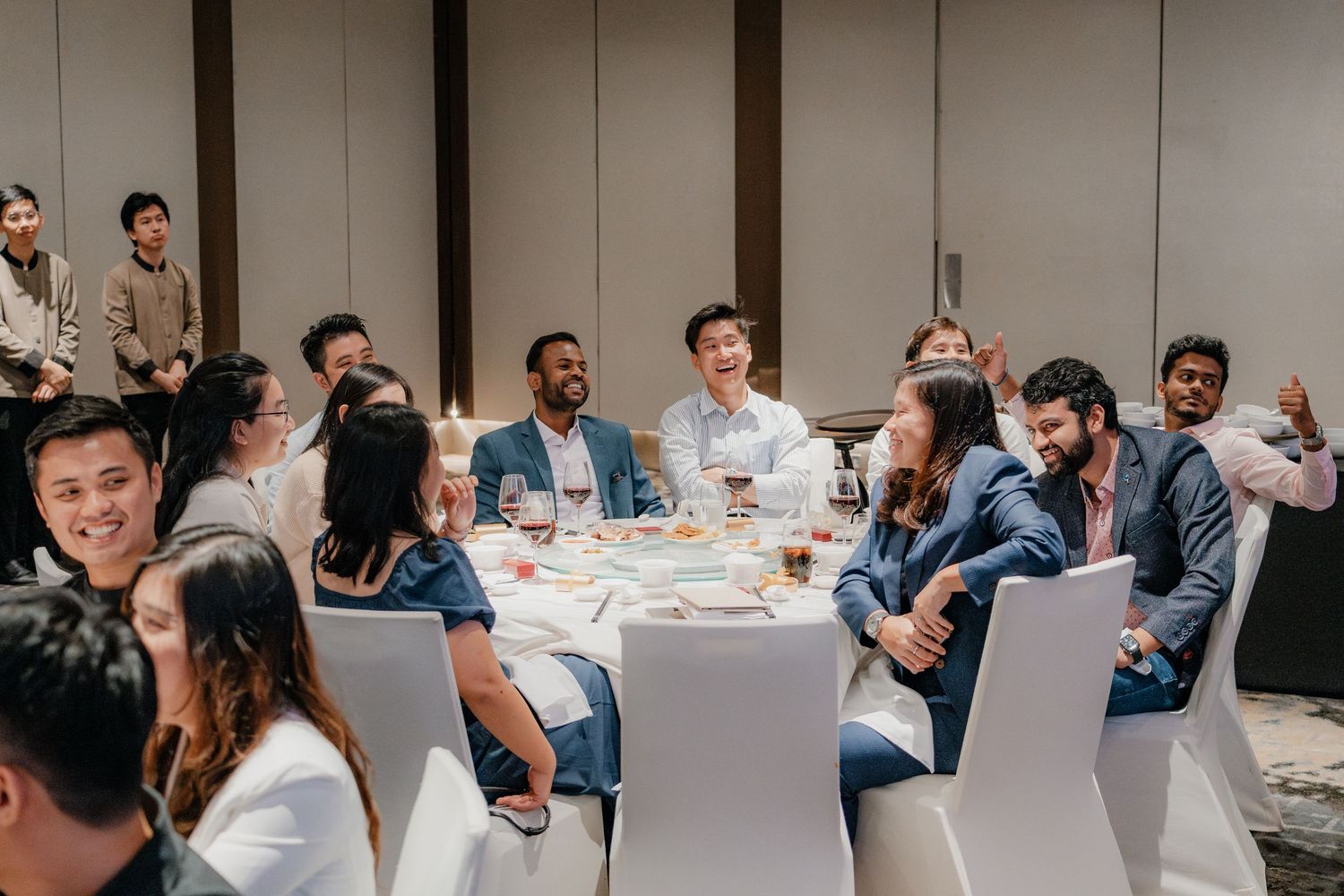 Wedding guests enjoy a lively reception dinner at elegantly set round tables in a modern banquet hall.
