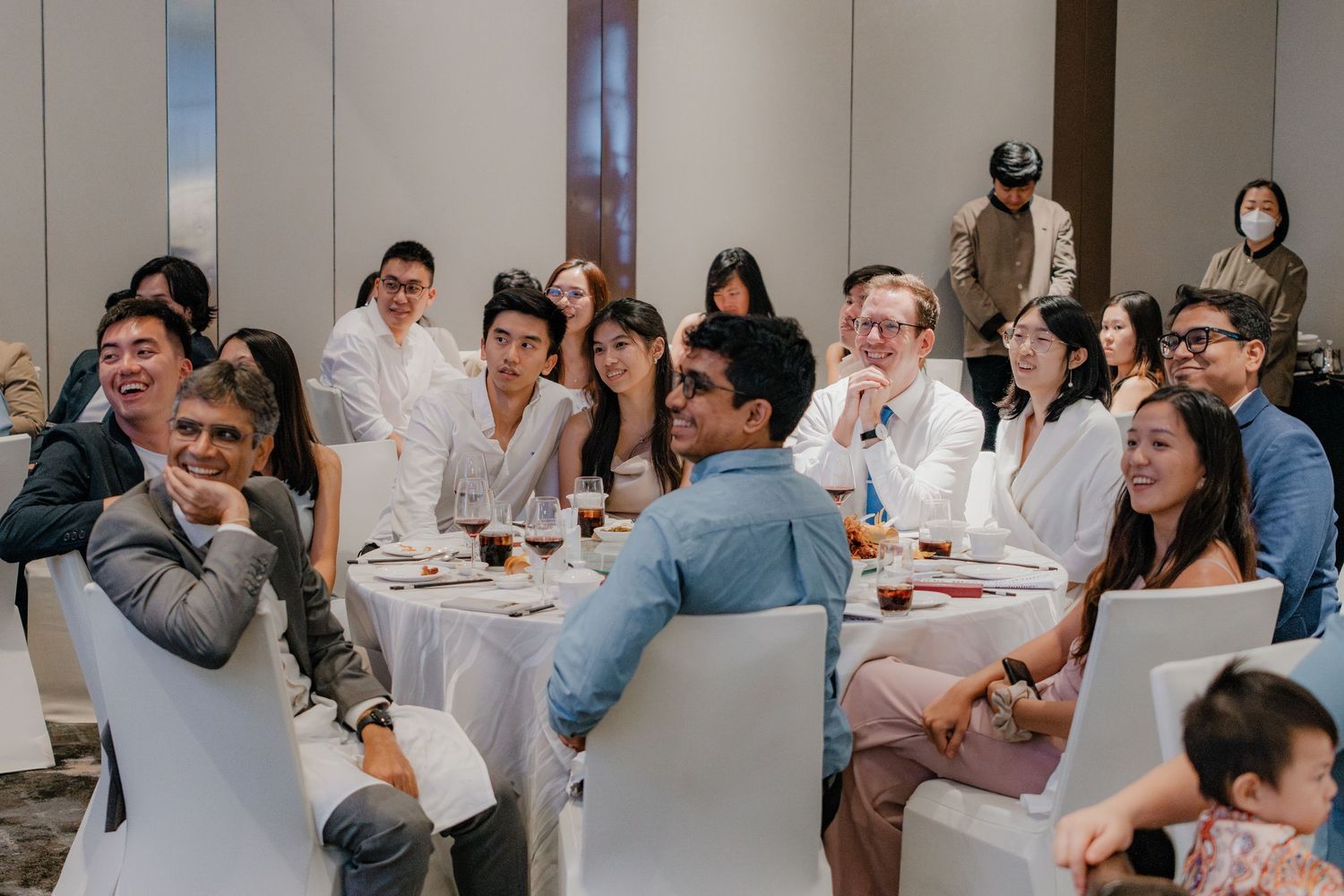 Wedding reception guests seated at round tables in a brightly lit banquet room.