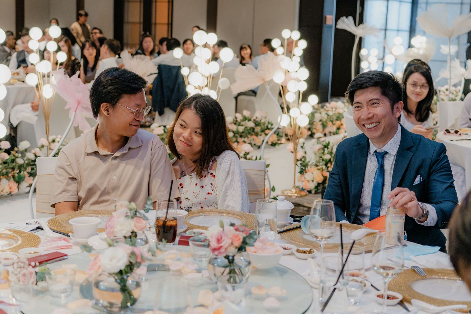 Wedding guests enjoying a meal at decorated tables with floral centerpieces.