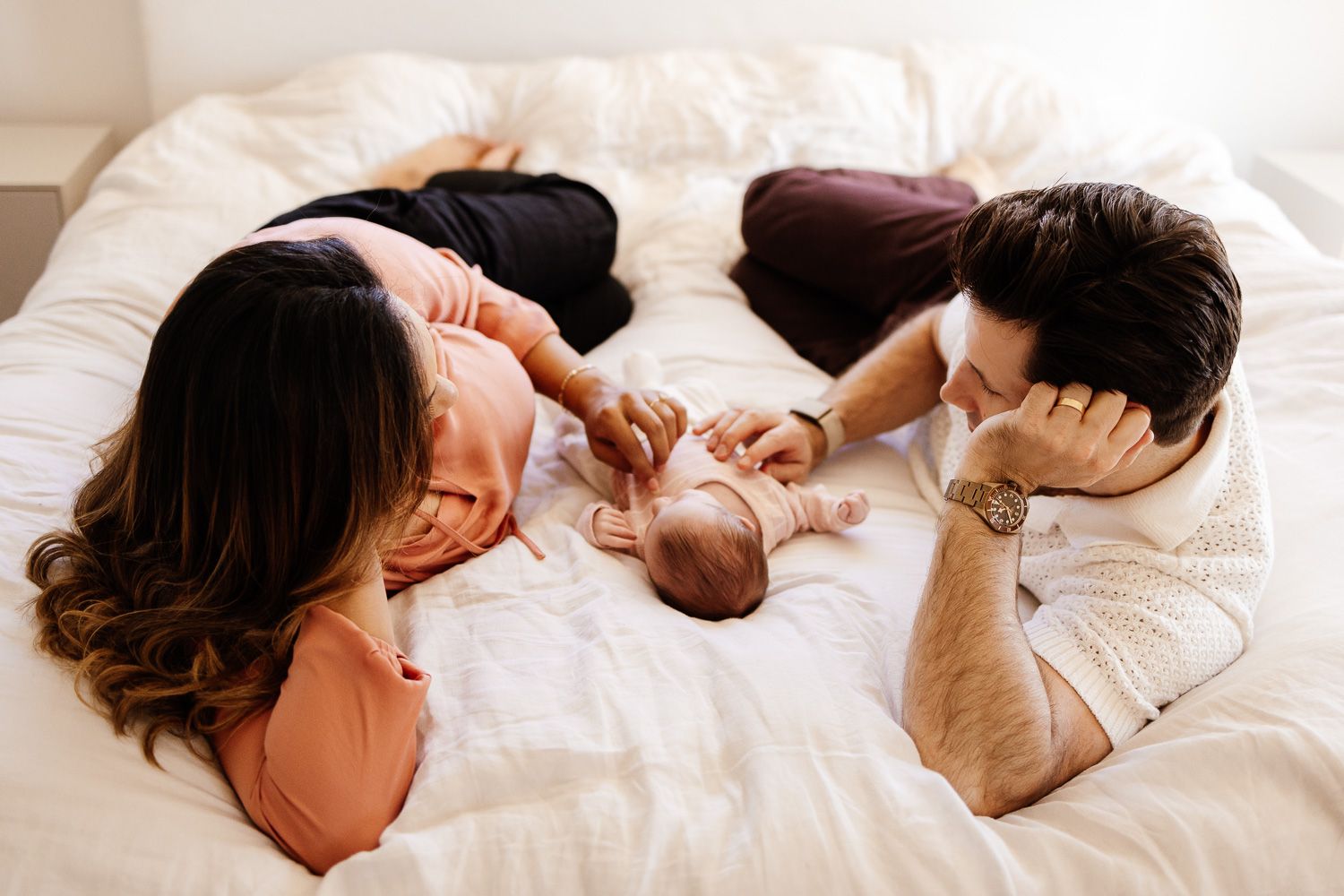Parents lay on their bed with their baby at their in-home Bay Area newborn photography session